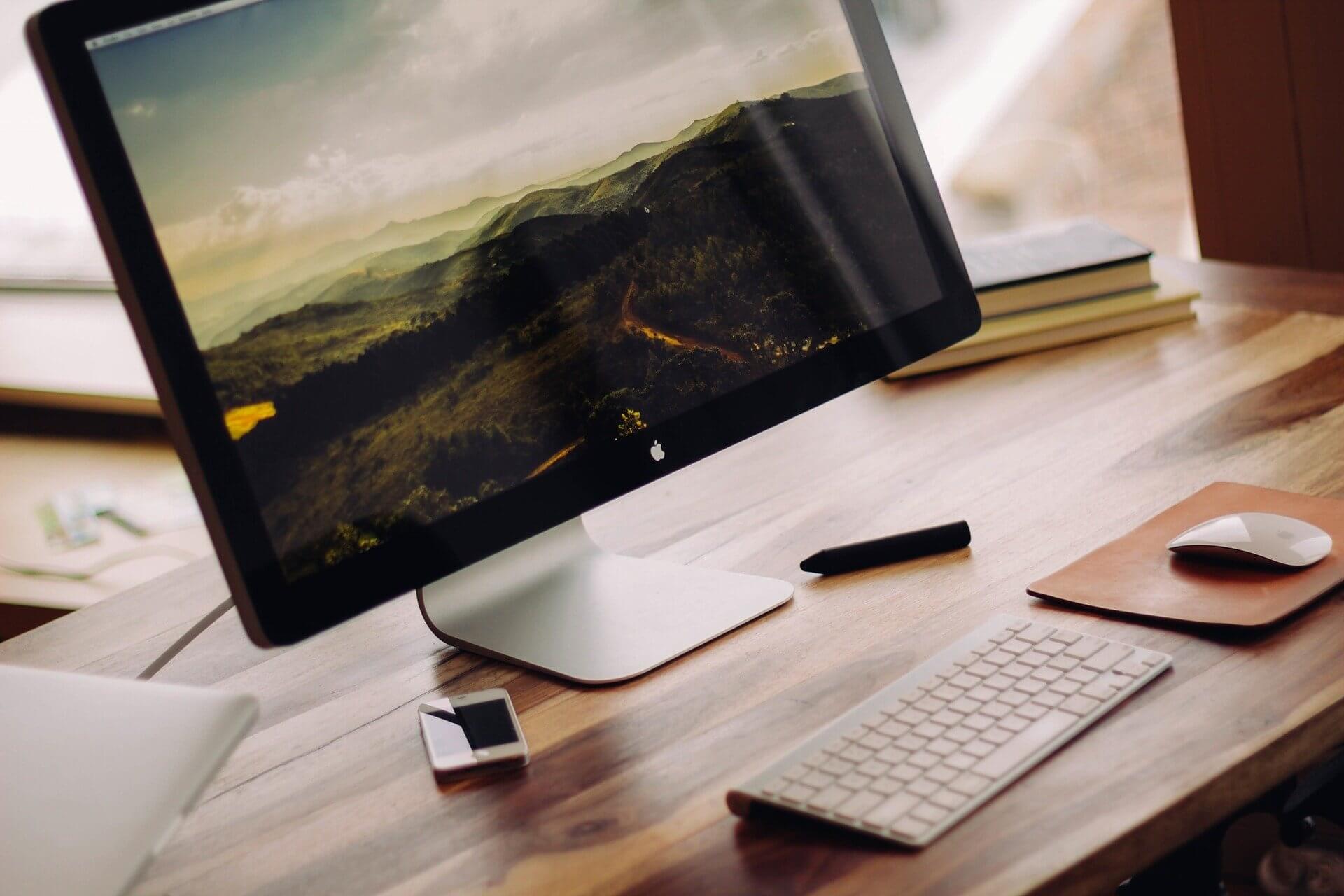 iMac auf einem Schreibtisch mit Büchern, Tastatur und Maus