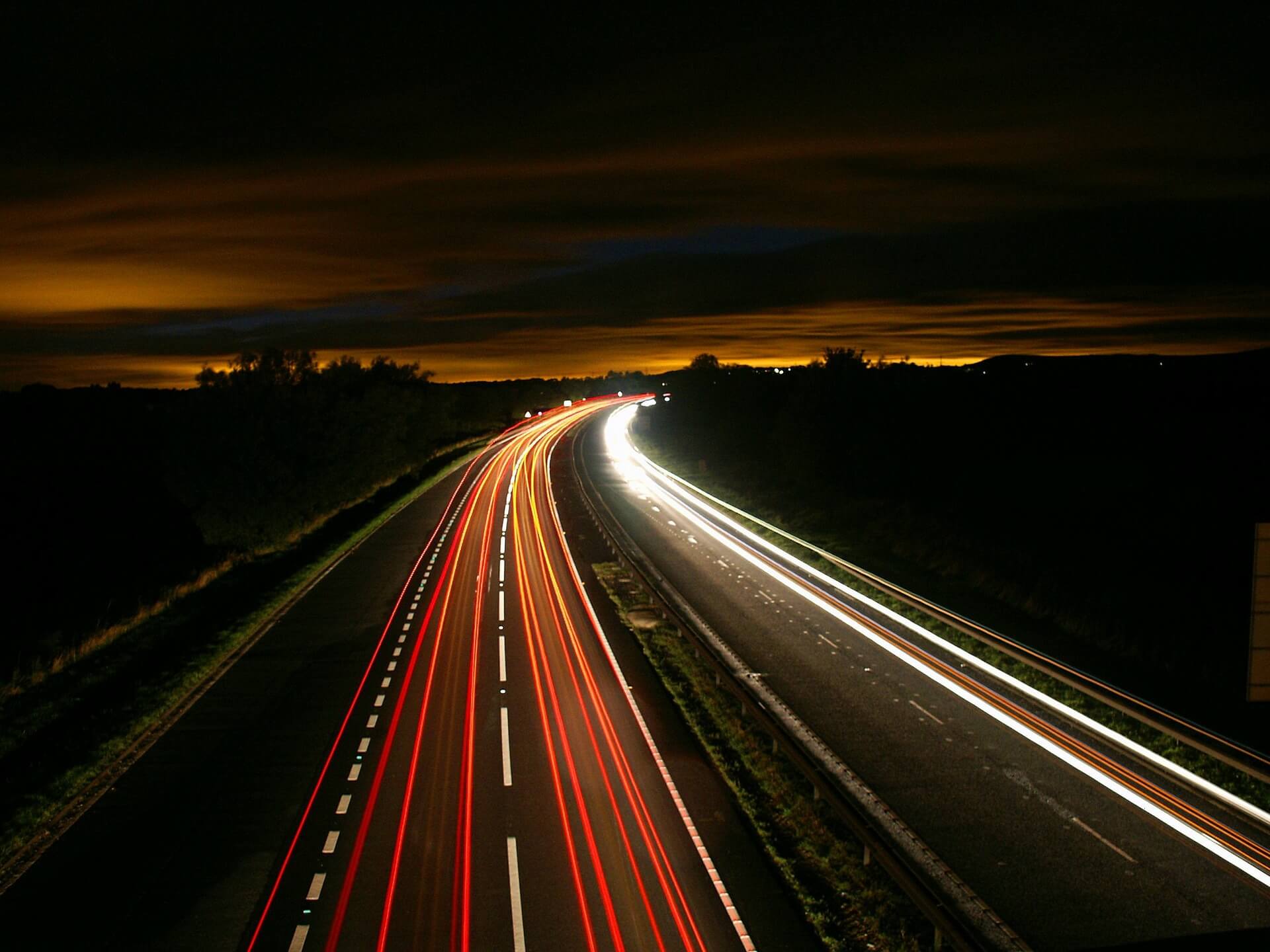 Autos auf einer Autobahn bei Nacht, durch Langzeitbelichtung sind nur rote und weiße Streifen sichtbar