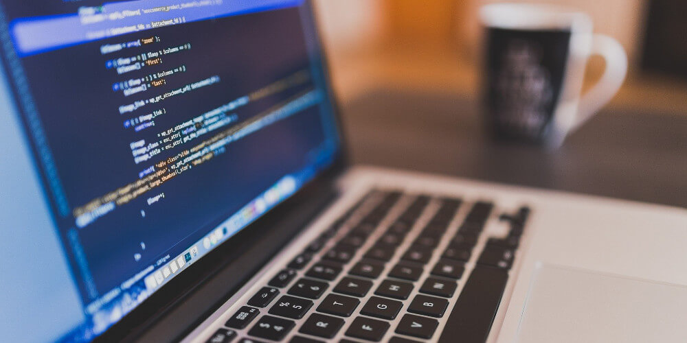 Coffee cup on a table next to a laptop with source code.