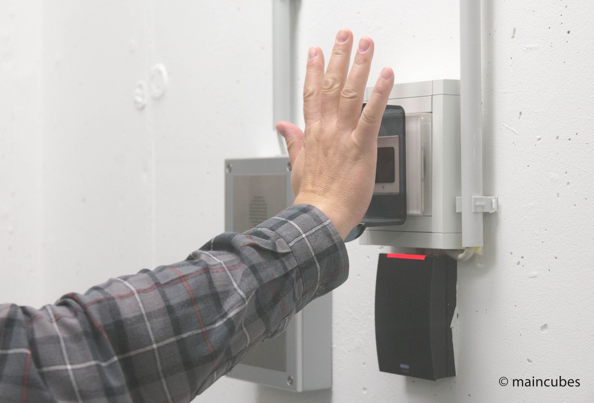 Hochmoderner Venenscanner an einer Wand montiert, davor eine Hand, welche die Handfläche offen zum Sensor zeigt.